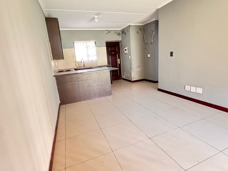 An open-plan living and kitchen area featuring tiled flooring and built-in cabinetry, currently requiring wall repairs and cosmetic updates.