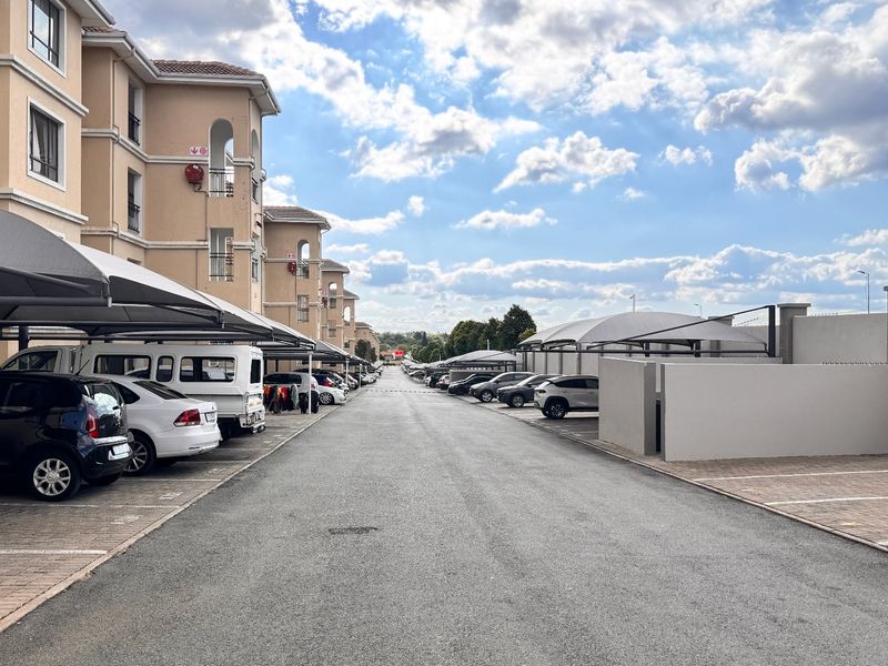 Exterior view of an apartment complex featuring a paved driveway, covered parking bays, and well-maintained building facades.