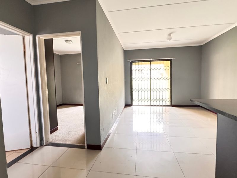 An open-plan living area featuring tiled flooring, a breakfast bar, and a sliding door with a security gate leading to the exterior.