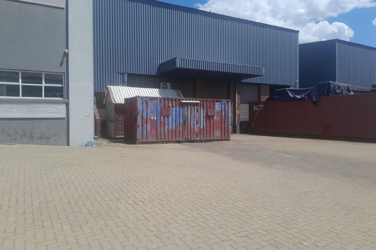 Rear exterior view of an industrial property featuring a paved yard, loading bay access with roller shutter doors, and corrugated metal cladding.
