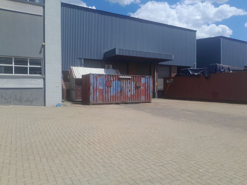 Rear exterior view of an industrial property featuring a paved yard, loading bay access with roller shutter doors, and corrugated metal cladding.