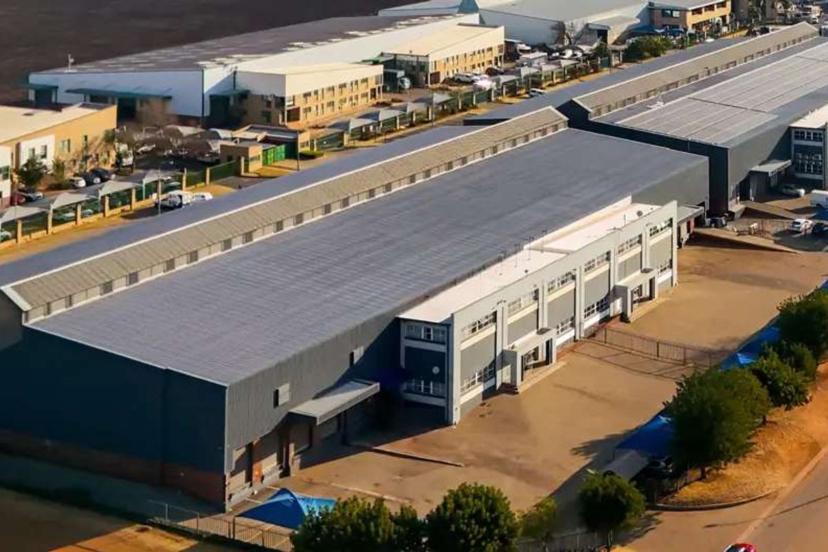 Aerial view of a large industrial warehouse facility featuring extensive metal roofing, loading bays, and a paved yard area within a business park.
