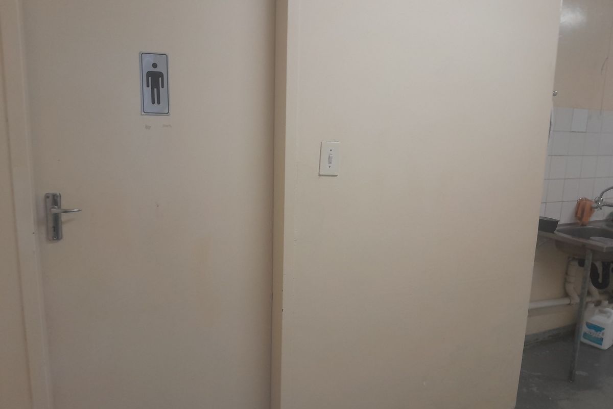 A functional industrial restroom area featuring a stainless steel sink, tiled splashback, and a designated door entrance.