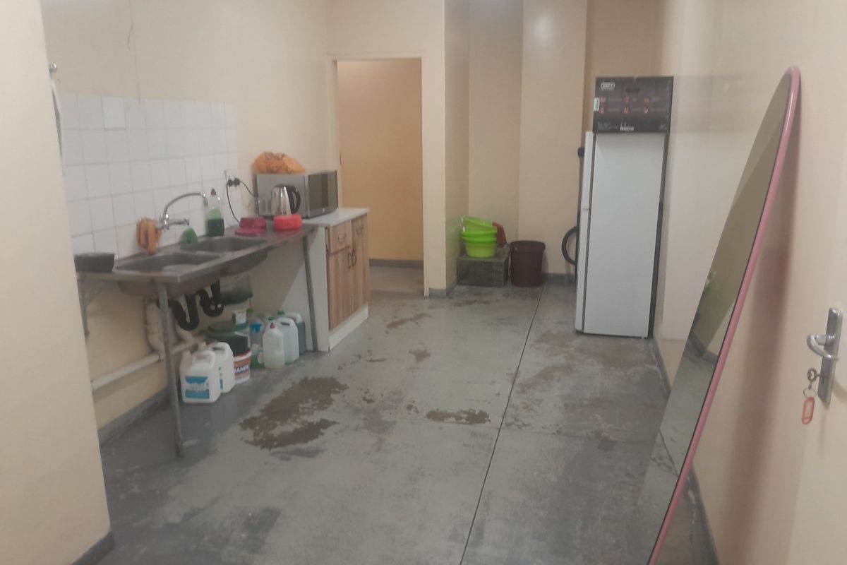 A functional industrial kitchen area featuring a stainless steel double sink, tiled splashback, and concrete flooring, suitable for utility or staff use.