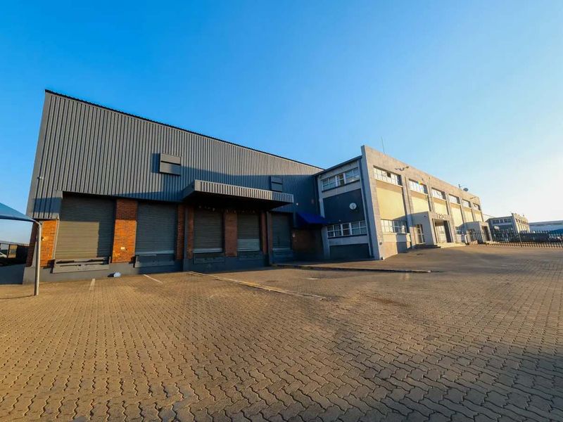 Industrial property exterior featuring multiple roller shutter loading bays, metal cladding facade, and a spacious paved driveway area.
