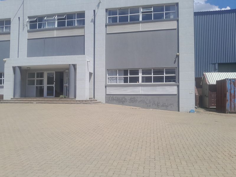 Front elevation of an industrial building featuring a paved driveway, covered entrance, and multi-pane windows with visible exterior wall staining.