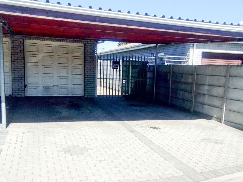 A paved driveway featuring a covered carport, secure metal gate, and a garage door, providing functional off-street parking for the property.
