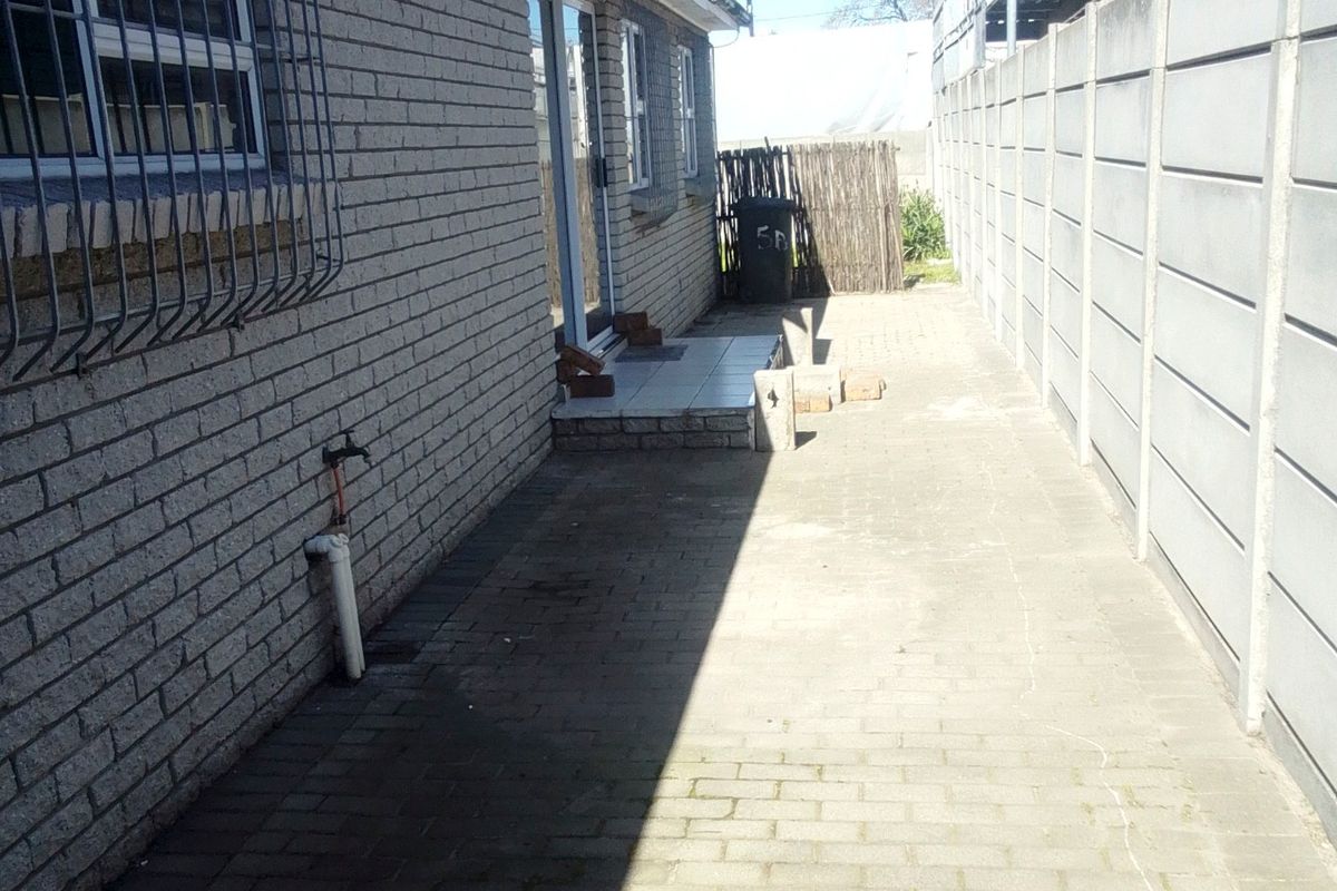 A side exterior view of the property featuring brick wall construction, security bars on windows, and a paved walkway enclosed by a precast concrete boundary wall.