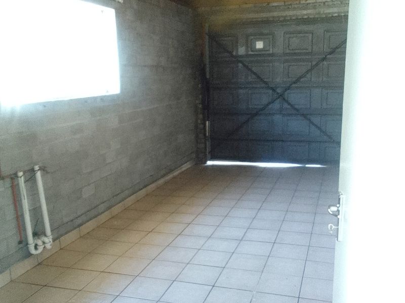 A spacious, unfinished garage featuring tiled flooring, exposed timber roof trusses, and exposed concrete block walls with visible plumbing connections.
