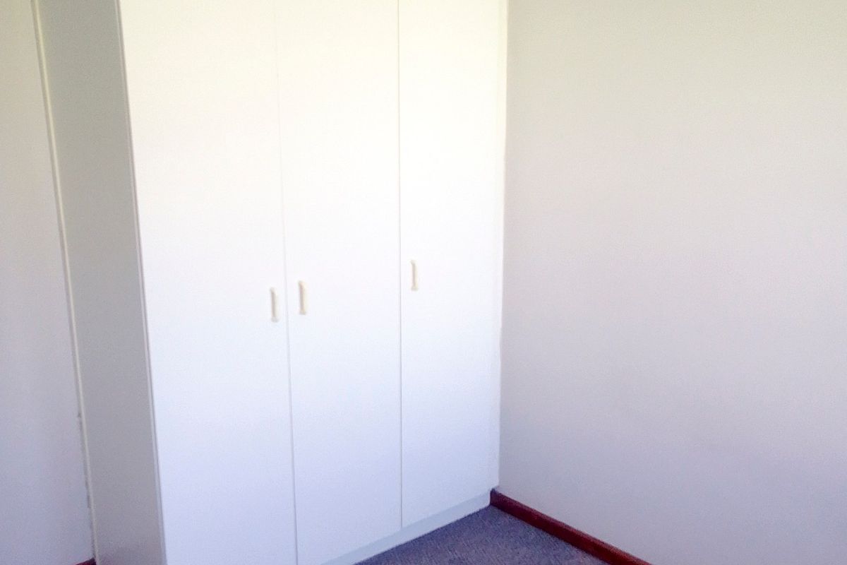 A vacant bedroom featuring built-in white cupboards, carpeted flooring, and neutral wall finishes, offering a clean canvas for personalization.