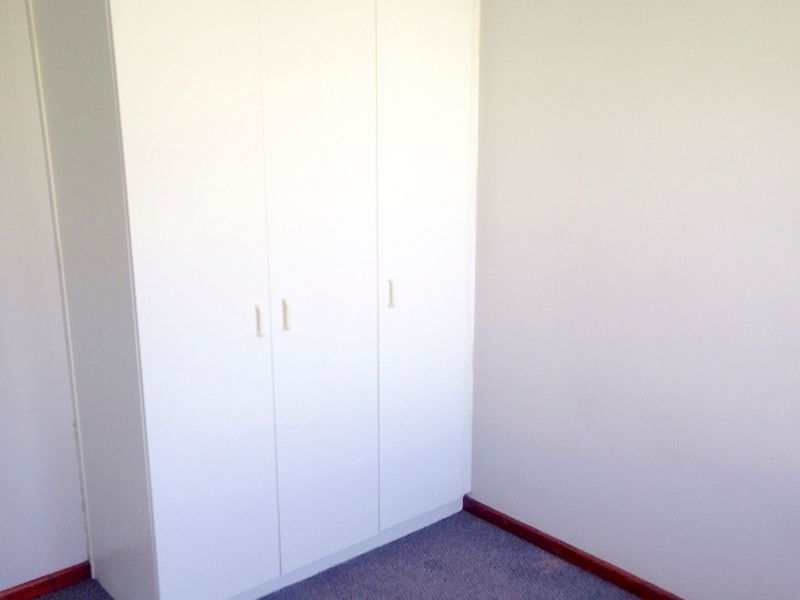 A vacant bedroom featuring built-in white cupboards, carpeted flooring, and neutral wall finishes, offering a clean canvas for personalization.
