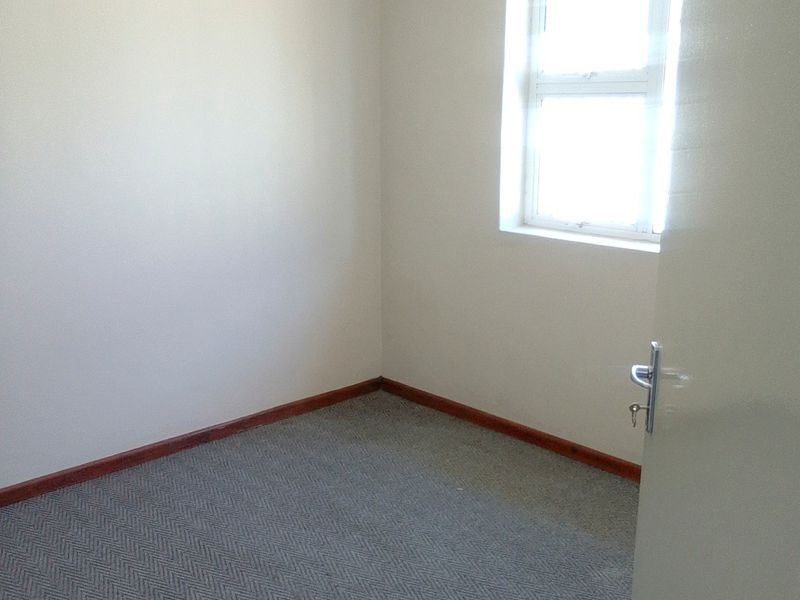 A clean, empty bedroom featuring neutral walls, carpeted flooring, and a window, providing a blank canvas for personalization.