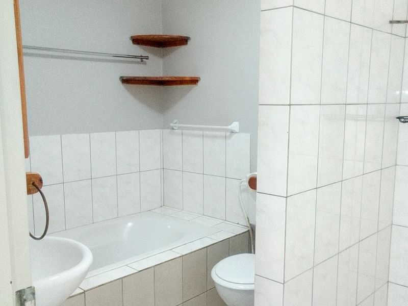 A functional bathroom featuring a built-in bathtub, toilet, wall-mounted basin, and a separate tiled shower enclosure with neutral wall tiling.