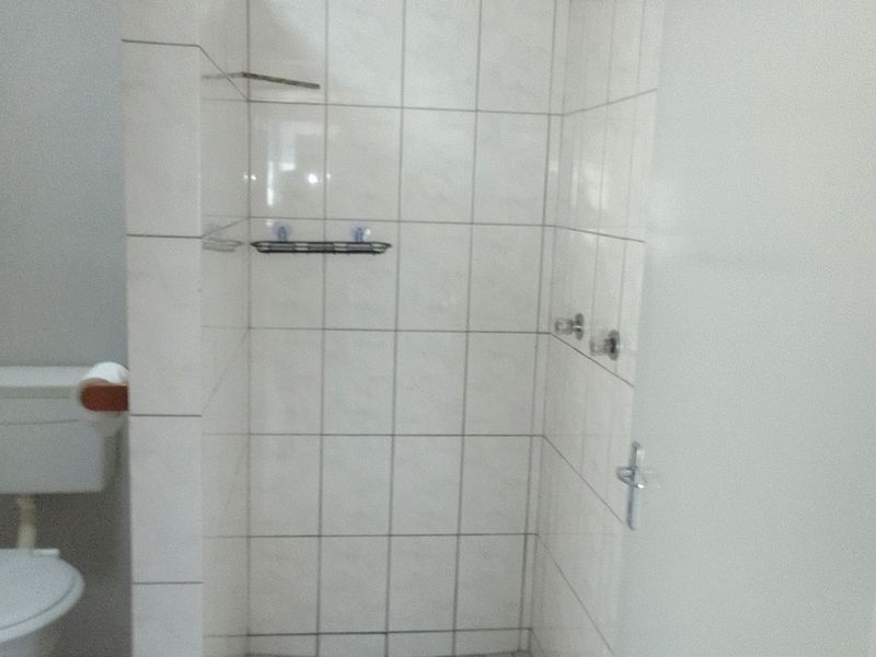 A functional bathroom featuring a tiled shower enclosure with a shower head and mixer, alongside a standard toilet.