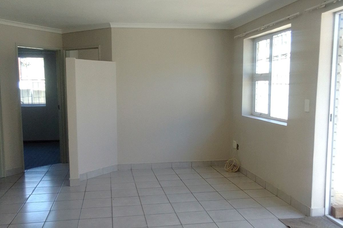 A bright, empty living area featuring neutral tiled flooring, a coved ceiling, and direct access to an outdoor space through a sliding door.