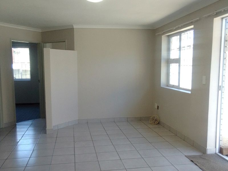 A bright, empty living area featuring neutral tiled flooring, a coved ceiling, and direct access to an outdoor space through a sliding door.