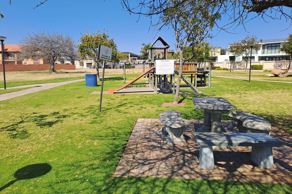 A communal garden area featuring a playground, stone picnic table with benches, and paved seating area within a residential estate.
