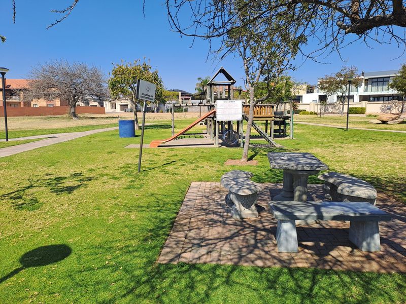 A communal garden area featuring a playground, stone picnic table with benches, and paved seating area within a residential estate.