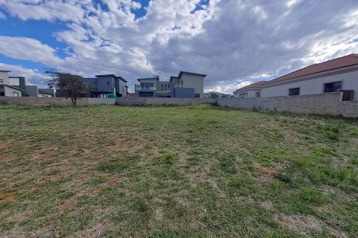 A vacant residential plot featuring a level grassed surface and enclosed by a perimeter boundary wall in a developed neighborhood.