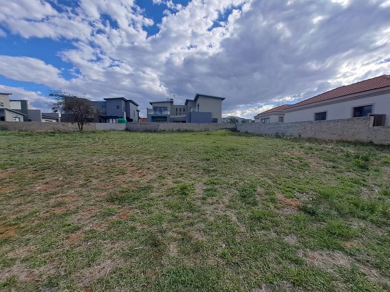 A vacant residential plot featuring a level grassed surface and enclosed by a perimeter boundary wall in a developed neighborhood.
