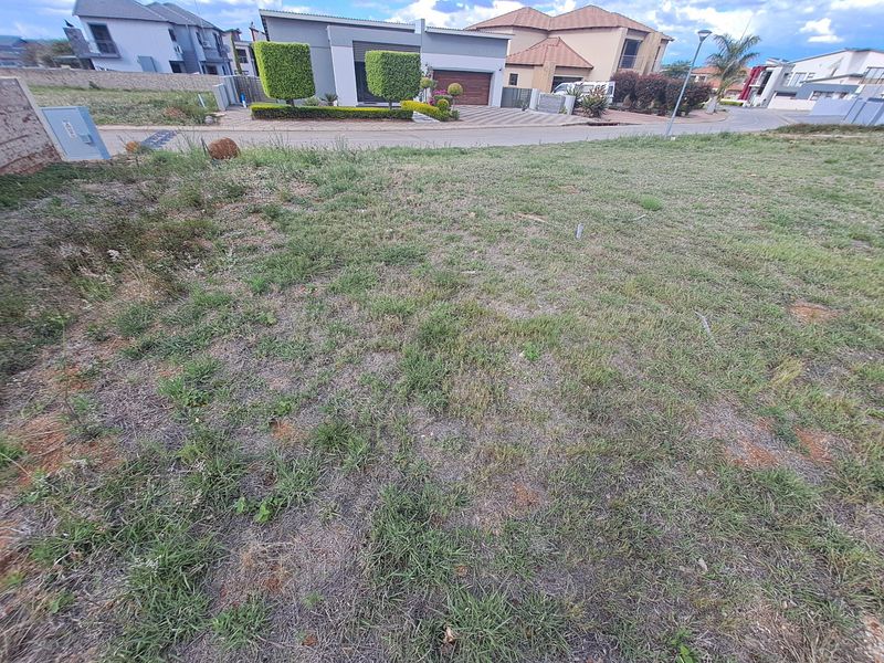 A vacant residential plot of land featuring grassed terrain and a utility connection point, situated in a developed suburban street.