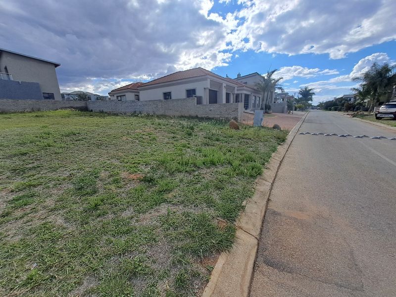 A vacant residential plot situated along a paved street with an existing boundary wall, offering a clear view of the surrounding neighborhood.
