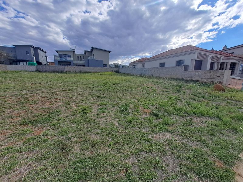 A vacant residential plot featuring a grassed surface and enclosed by a perimeter boundary wall, situated within a developed residential estate.