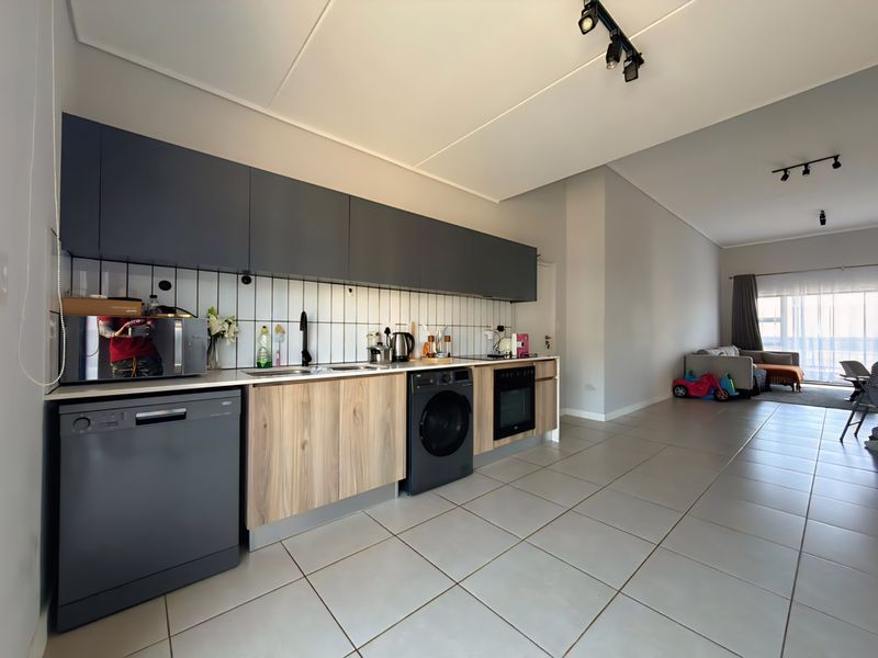 Modern open-plan kitchen featuring sleek two-tone cabinetry, integrated appliances, subway tile backsplash, and neutral tiled flooring, flowing into a bright living area.