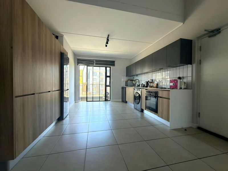 Modern kitchen featuring sleek wood-tone and dark cabinetry, tiled flooring, integrated oven, and a subway tile backsplash, leading to a private balcony.
