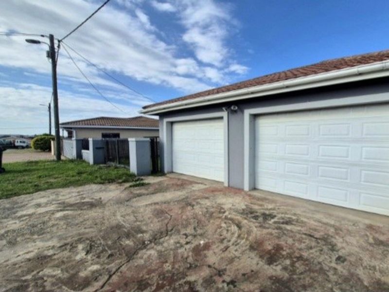 Exterior view of a double garage with white sectional doors and a concrete driveway showing signs of wear.