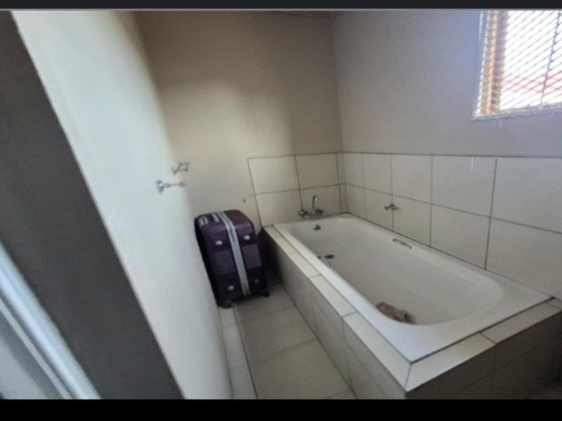 A functional bathroom featuring a built-in bathtub with tiled surround and splashback, providing a clean and practical space.
