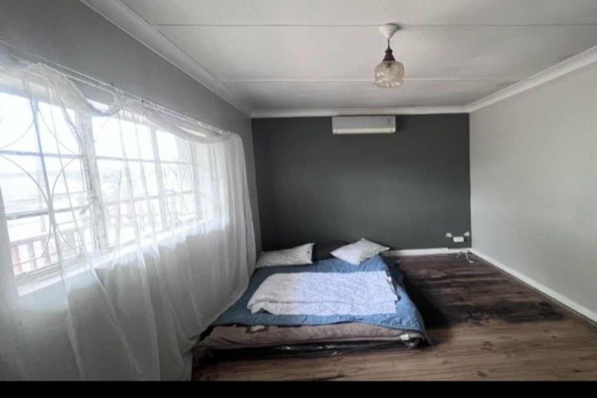 A bedroom featuring laminate flooring, a wall-mounted air conditioning unit, and a neutral color scheme with a dark accent wall.