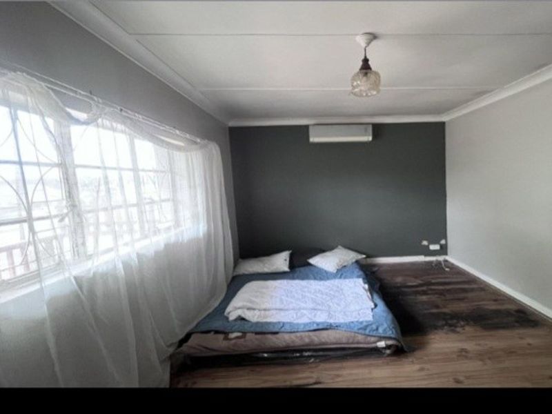 A bedroom featuring laminate flooring, a wall-mounted air conditioning unit, and a neutral color scheme with a dark accent wall.