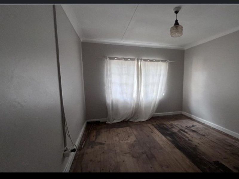 An empty bedroom featuring original timber flooring, coved cornicing, and surface-mounted electrical conduit, requiring cosmetic updates to restore its appeal.