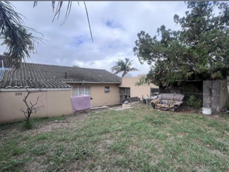 Rear view of the property showing the back facade, tiled roof, and garden area with mature trees.
