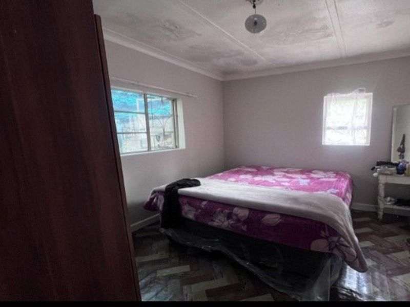 A bedroom featuring tiled flooring, ceiling cornice, and security bars on the windows. The room shows signs of wear and requires cosmetic updates.