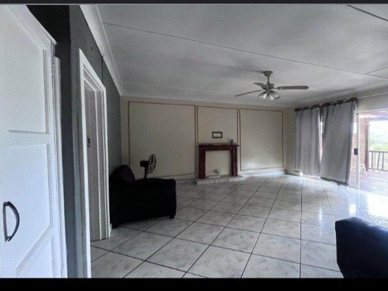 Spacious living room featuring tiled flooring, a central fireplace, ceiling fan, and sliding glass doors leading to an outdoor area.