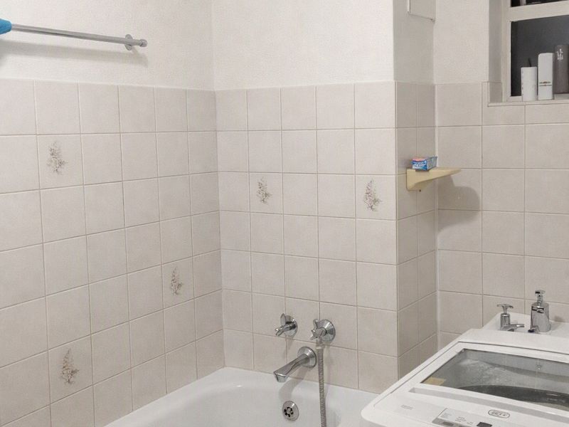 A functional bathroom featuring a built-in bathtub with chrome fixtures, tiled walls, and a window with security bars.