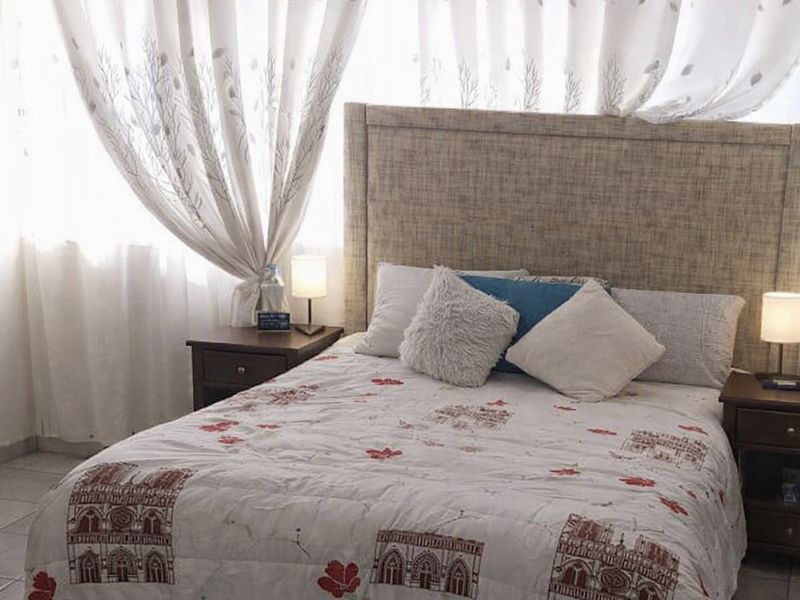 A bedroom featuring tiled flooring and a central ceiling light fixture, with large windows covered by curtains.