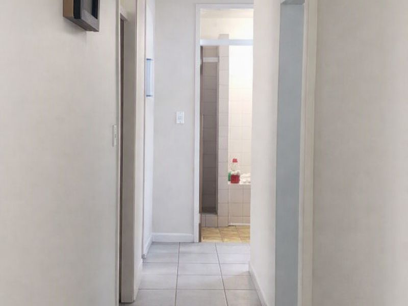 A clean, neutral hallway with tiled flooring leading towards a bathroom area, featuring simple architectural lines and standard door frames.