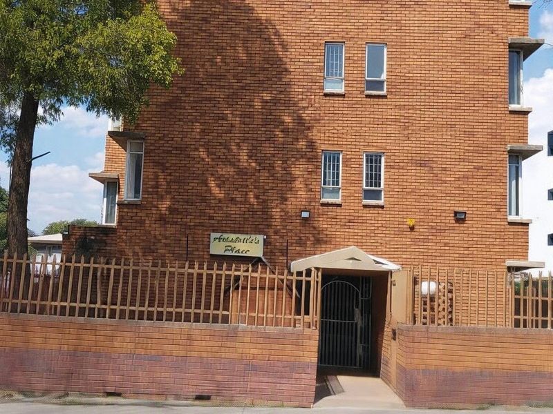 Front elevation of a multi-story brick apartment building featuring a secure gated entrance and perimeter fencing.