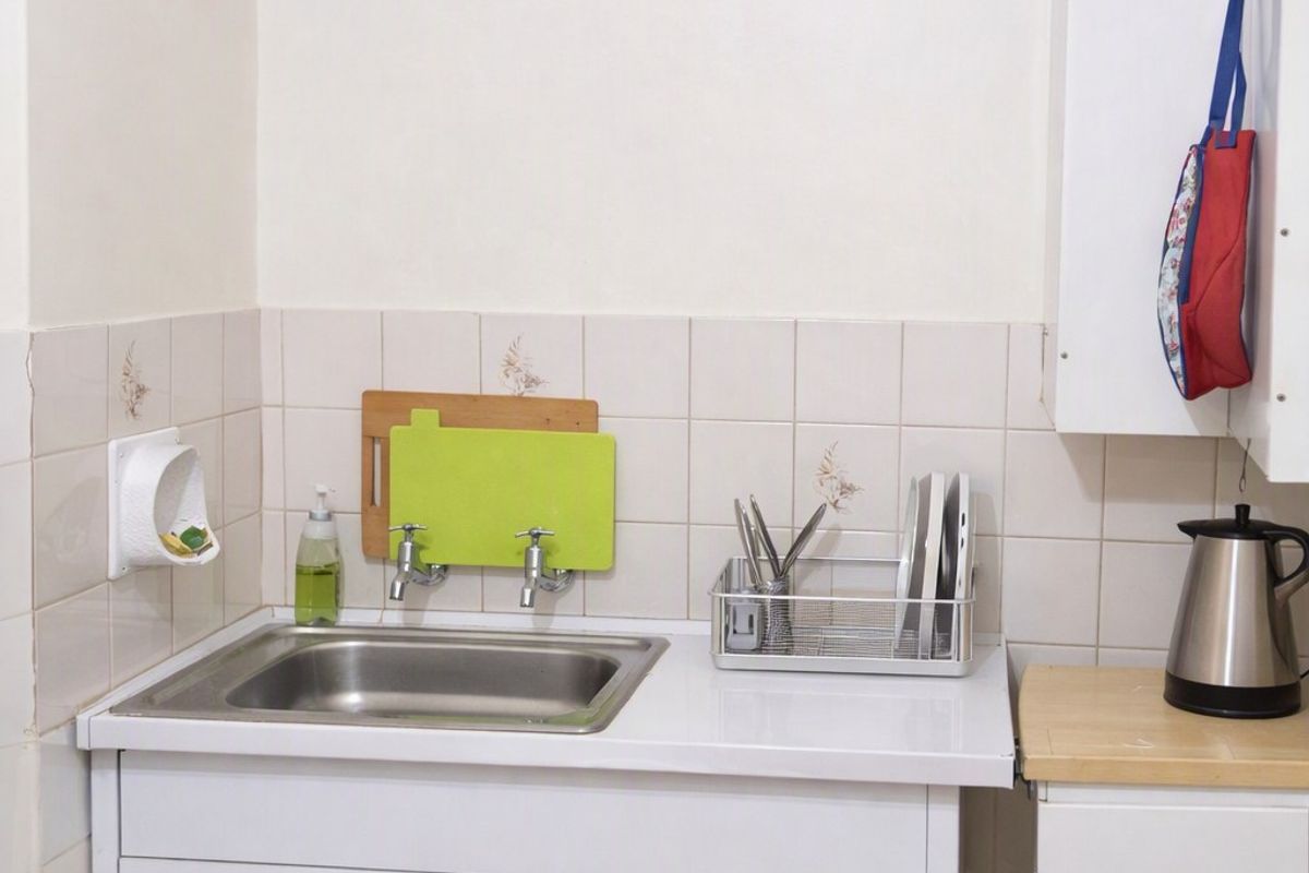 A compact kitchen area featuring a stainless steel sink, tiled splashback, and functional built-in cabinetry with laminate countertops.