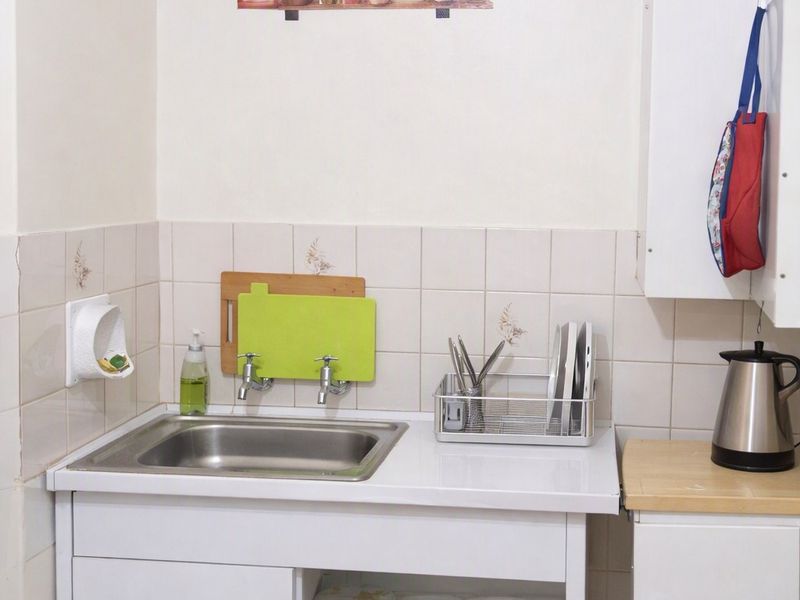 A compact kitchen area featuring a stainless steel sink, tiled splashback, and functional built-in cabinetry with laminate countertops.