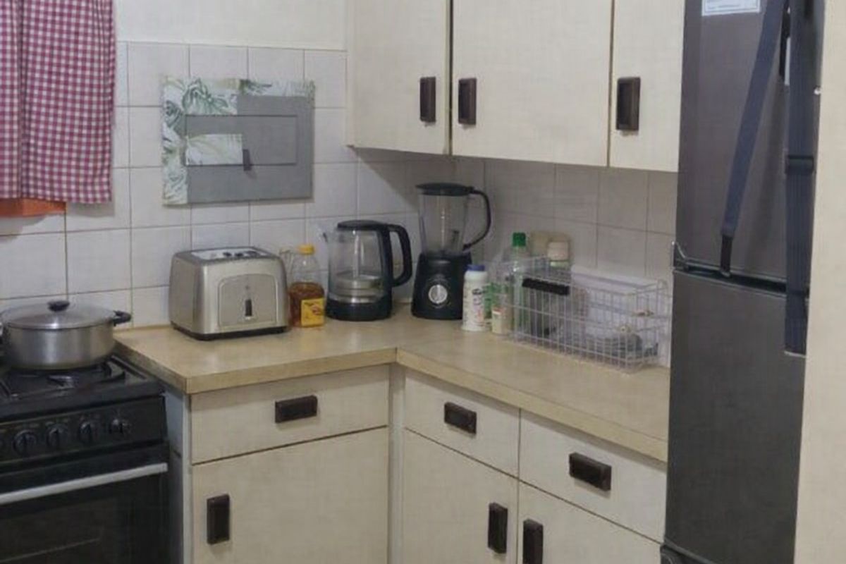 A compact kitchen featuring dated cabinetry, laminate countertops, and tiled finishes, offering potential for a modern renovation.