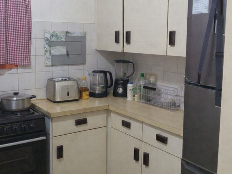 A compact kitchen featuring dated cabinetry, laminate countertops, and tiled finishes, offering potential for a modern renovation.