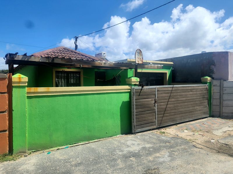 Front exterior view of a single-story house featuring a bright green boundary wall, sliding gate, and a weathered wooden pergola structure.