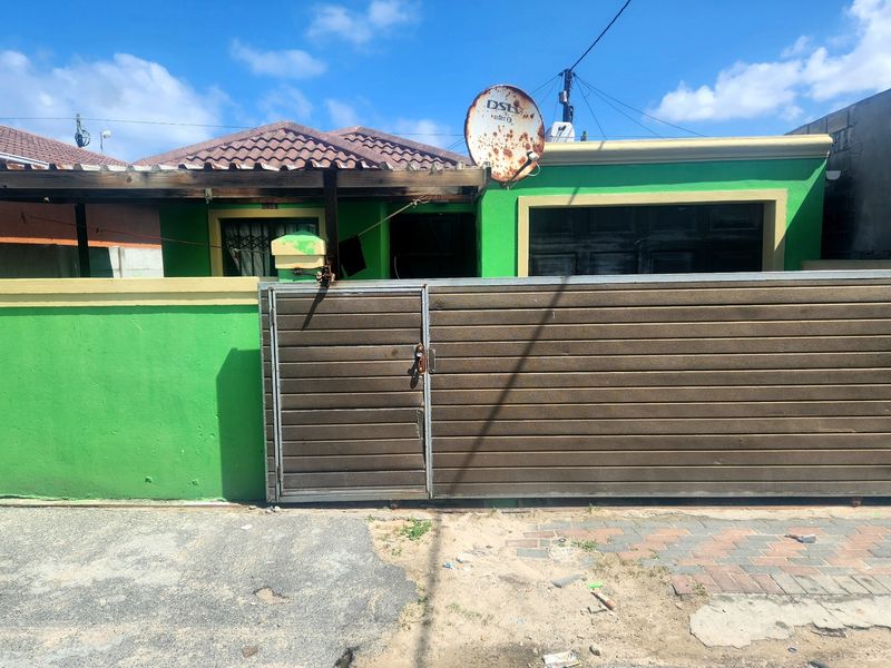 Front view of a residential property featuring a sliding gate, boundary wall, and attached garage with a tiled roof structure.