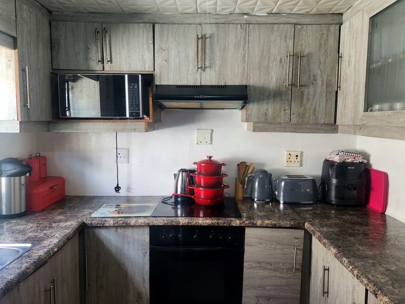 A compact kitchen featuring wood-look laminate cabinetry, a built-in oven with hob, and a stainless steel sink, requiring some cosmetic updates.