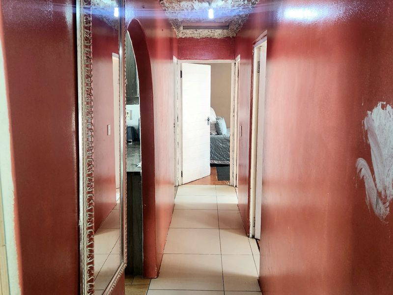 A narrow hallway featuring tiled flooring, an arched entryway, and a textured ceiling, leading towards adjacent rooms.