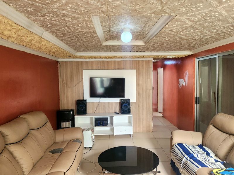 Living room featuring tiled flooring, textured ceiling, and wood-look wall paneling. The space requires cosmetic updates to the walls and ceiling finishes.